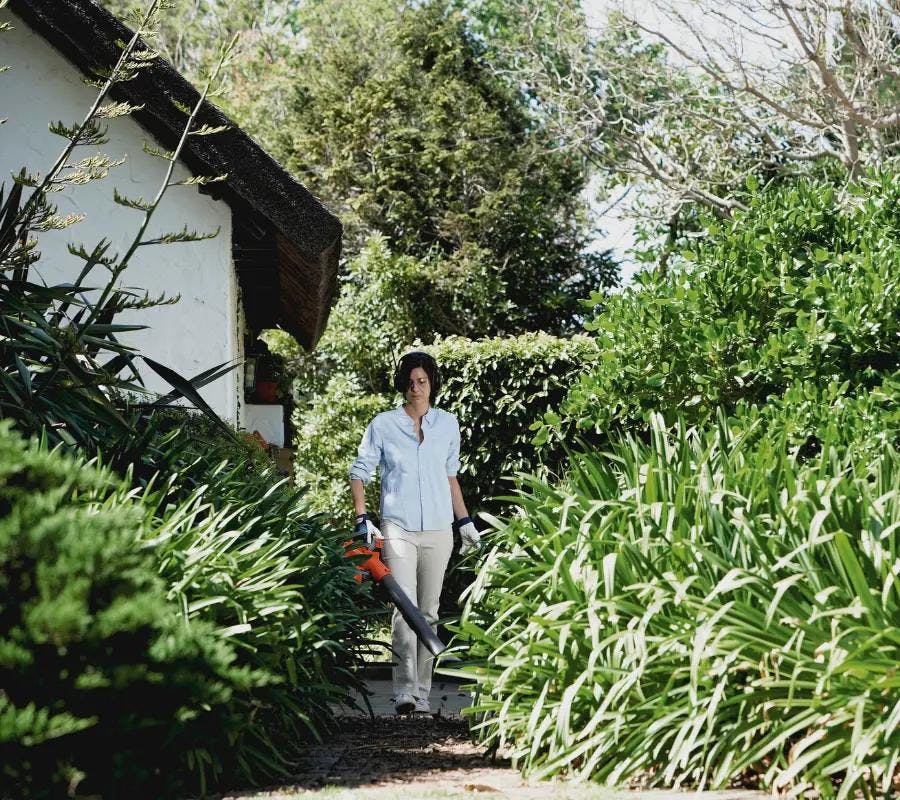 woman with leaf blower in leafy backyard